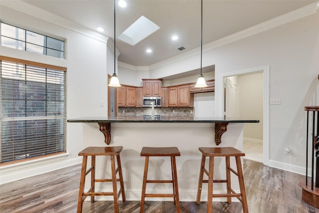 2132 Portwood Way, Fort Worth, TX 76179 - kitchen with stainless steel microwave, crown molding, a skylight, backsplash, and a kitchen breakfast bar