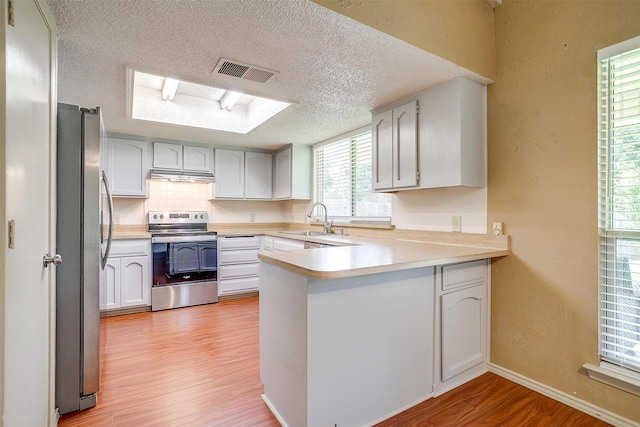 6436 Meadowlark Ln E, Watauga, TX 76148 - kitchen featuring stainless steel appliances, a peninsula, a sink, a textured ceiling, and light wood-style flooring