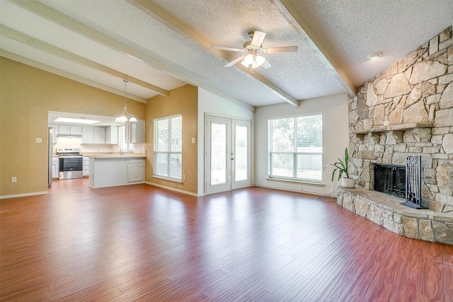 6436 Meadowlark Ln E, Watauga, TX 76148 - unfurnished living room with a textured ceiling, a stone fireplace, plenty of natural light, baseboards, and wood finished floors
