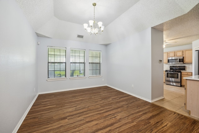 unfurnished dining area featuring light wood-style flooring, a chandelier, a textured ceiling, baseboards, and a ceiling fan