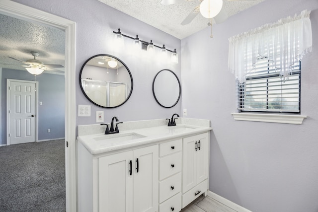 full bath featuring ceiling fan, a textured ceiling, baseboards, and double vanity