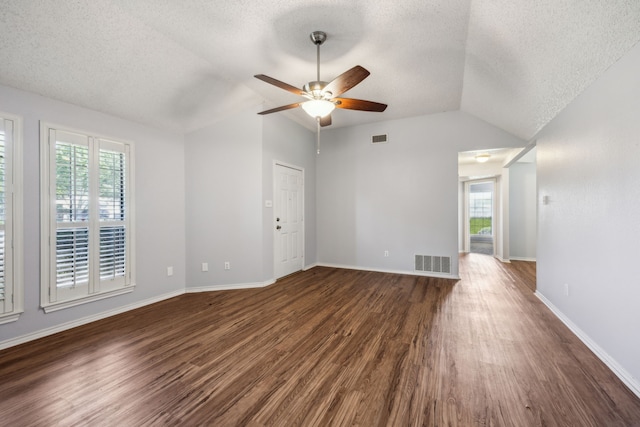 empty room featuring vaulted ceiling, a textured ceiling, healthy amount of natural light, dark wood-type flooring, and a ceiling fan