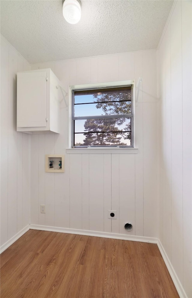 125 Harrison, Detroit, TX 75436 - washroom with light wood-style flooring, cabinet space, washer hookup, a textured ceiling, and a decorative wall