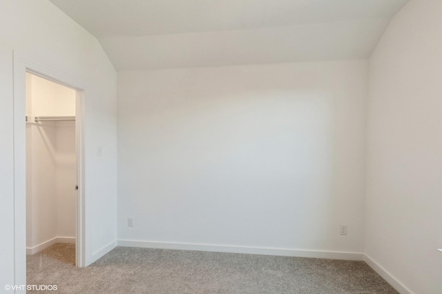 unfurnished bedroom featuring a spacious closet, light colored carpet, vaulted ceiling, a closet, and baseboards