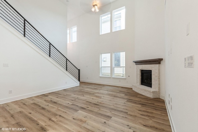 unfurnished living room featuring plenty of natural light, stairs, wood finished floors, a high ceiling, and a fireplace