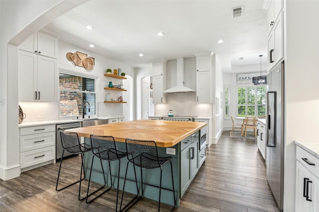 5900 Stage Coach Cir, Westlake, TX 76262 - kitchen featuring butcher block countertops, appliances with stainless steel finishes, wall chimney exhaust hood, a breakfast bar area, and arched walkways