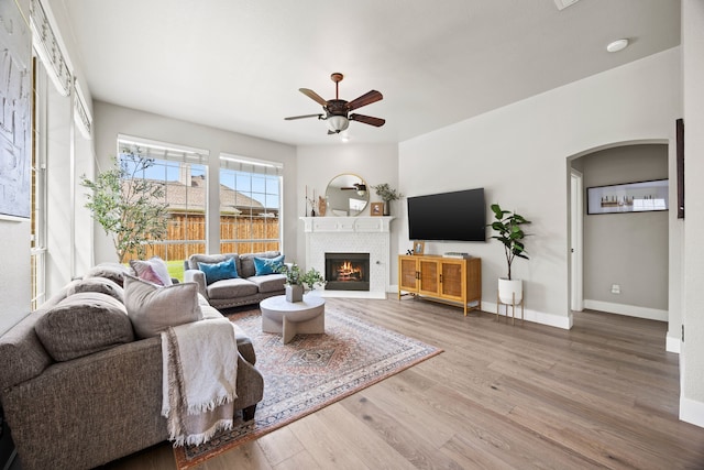 2441 Deerwood Dr, Little Elm, TX 75068 - living room featuring ceiling fan, wood finished floors, baseboards, a brick fireplace, and arched walkways