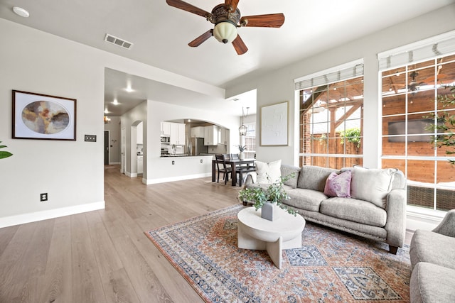 2441 Deerwood Dr, Little Elm, TX 75068 - living area with arched walkways, ceiling fan, light wood finished floors, and baseboards