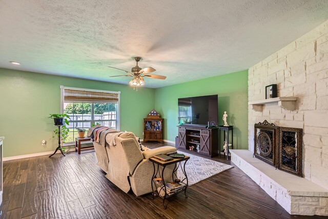 5225 Marks Cir, The Colony, TX 75056 - living room featuring a ceiling fan, dark wood-type flooring, a fireplace, a textured ceiling, and baseboards