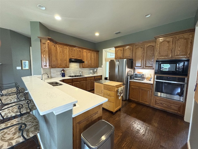 519 Butternut Dr, Garland, TX 75044 - kitchen featuring stainless steel appliances, under cabinet range hood, a sink, a peninsula, and dark wood finished floors