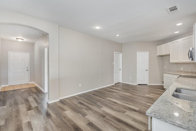 2109 Northridge Dr, Forney, TX 75126 - kitchen with arched walkways, wood finished floors, white cabinetry, light stone counters, and baseboards