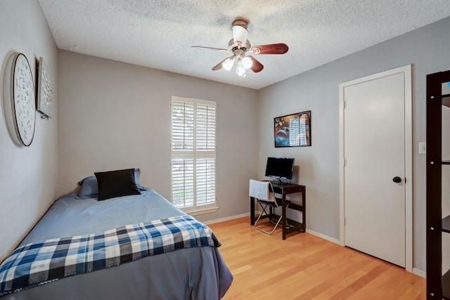 bedroom with light wood-style floors, a textured ceiling, a ceiling fan, and baseboards