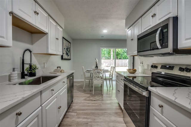 2209 Sheriff Dr, Grand Prairie, TX 75051 - kitchen featuring stainless steel appliances, a sink, white cabinets, light wood-style floors, and a textured ceiling