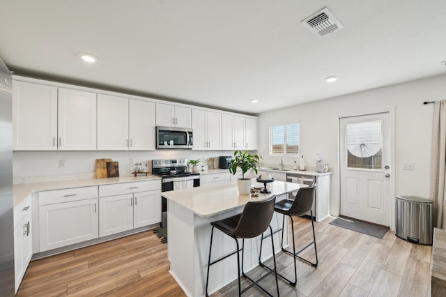 1229 Autumn Mist Ln, Forney, TX 75126 - kitchen featuring appliances with stainless steel finishes, white cabinets, a breakfast bar, light wood-type flooring, and light countertops