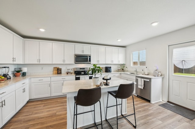 1229 Autumn Mist Ln, Forney, TX 75126 - kitchen featuring appliances with stainless steel finishes, white cabinetry, a kitchen breakfast bar, light wood finished floors, and light countertops