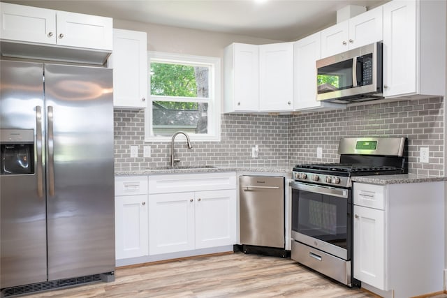 409 Forby Ave, Fort Worth, TX 76103 - kitchen with appliances with stainless steel finishes, a sink, white cabinetry, light wood-type flooring, and light stone counters