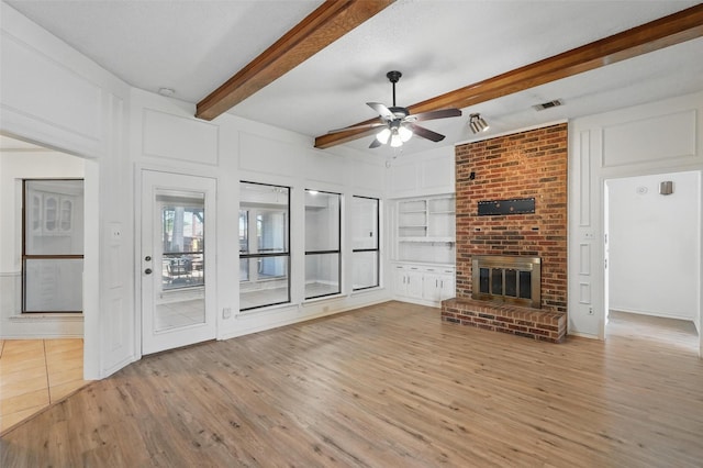 1027 Ridgeview Cir, Carrollton, TX 75007 - unfurnished living room featuring beamed ceiling, light wood-type flooring, ceiling fan, a fireplace, and a decorative wall