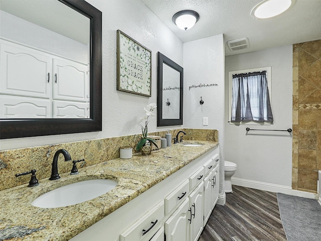 5433 Greenwood Way N, Richland Hills, TX 76180 - bathroom featuring toilet, double vanity, wood finished floors, baseboards, and a textured ceiling