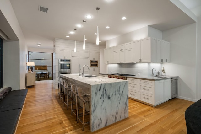3723 Gilbert Ave, Dallas, TX 75219 - kitchen featuring a sink, double oven, light wood finished floors, a breakfast bar area, and recessed lighting