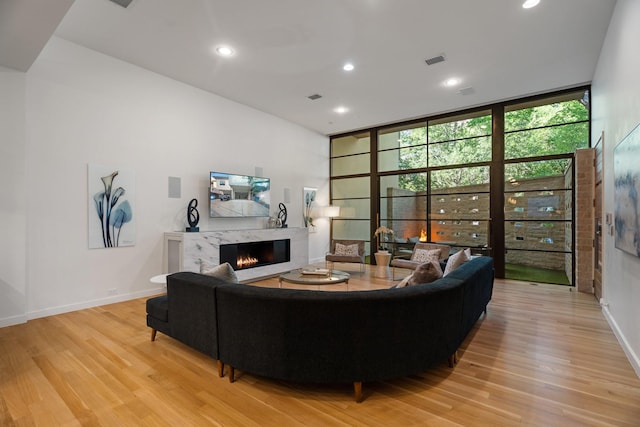 3723 Gilbert Ave, Dallas, TX 75219 - living room featuring light wood-style flooring, a high end fireplace, a wall of windows, recessed lighting, and baseboards