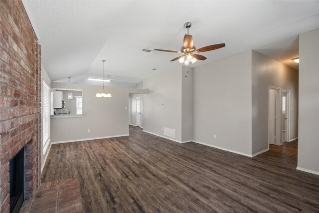 1133 Rosewood Ln, Lancaster, TX 75146 - unfurnished living room featuring a ceiling fan, dark wood finished floors, a fireplace, lofted ceiling, and a chandelier