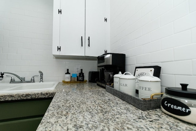 kitchen view of a sink, tasteful backsplash, white cabinets, light stone counters, and tile walls