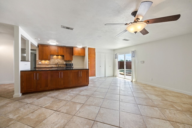 kitchen featuring dark countertops, backsplash, ceiling fan, light tile patterned flooring, and baseboards