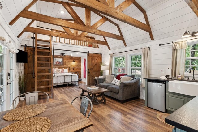 168 Barker Ln, Waco, TX 76705 - living area featuring a barn door, wooden walls, wood finished floors, high vaulted ceiling, and beam ceiling