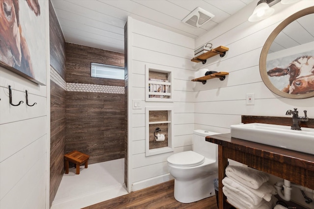 168 Barker Ln, Waco, TX 76705 - bathroom with a tile shower, toilet, wood finished floors, wooden walls, and vanity