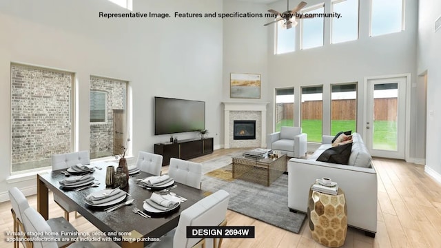 705 Arden Ln, Celina, TX 75009 - living room with a high ceiling, a ceiling fan, a glass covered fireplace, light wood-style flooring, and baseboards