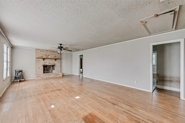 unfurnished living room featuring attic access, a ceiling fan, a textured ceiling, a fireplace, and light wood-style floors