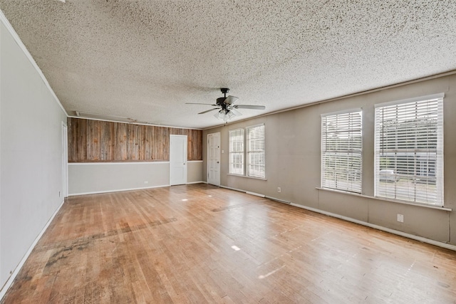 empty room with ceiling fan, wood finished floors, a textured ceiling, baseboards, and wood walls