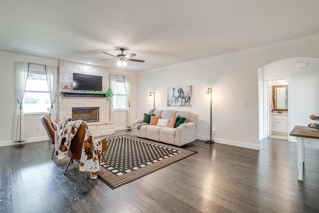 340 Sanger Dr, Springtown, TX 76082 - living room featuring arched walkways, a ceiling fan, dark wood-type flooring, a stone fireplace, and crown molding