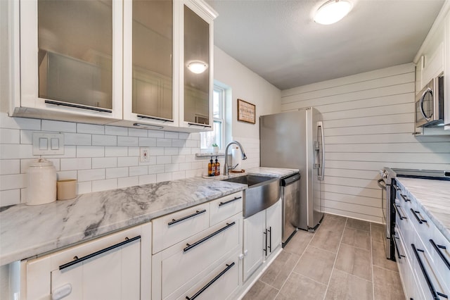 kitchen with stainless steel appliances, a sink, tasteful backsplash, light stone counters, and white cabinetry