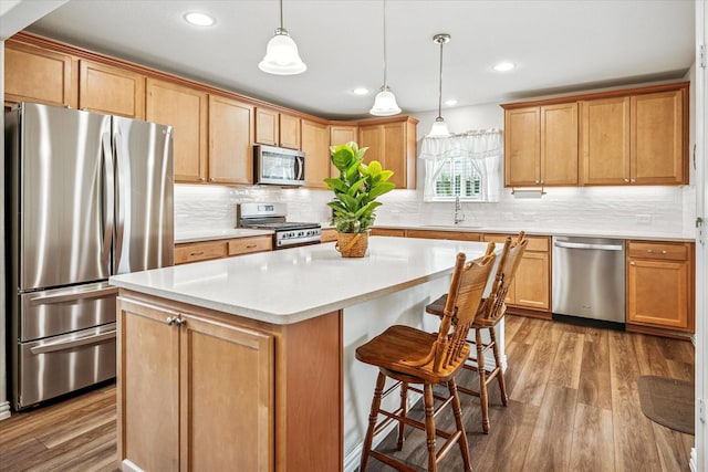 kitchen featuring appliances with stainless steel finishes, a kitchen island, a sink, wood finished floors, and recessed lighting