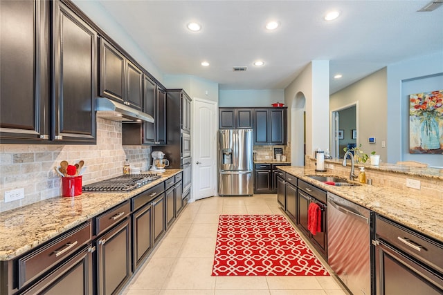 kitchen with appliances with stainless steel finishes, a sink, under cabinet range hood, decorative backsplash, and light tile patterned floors