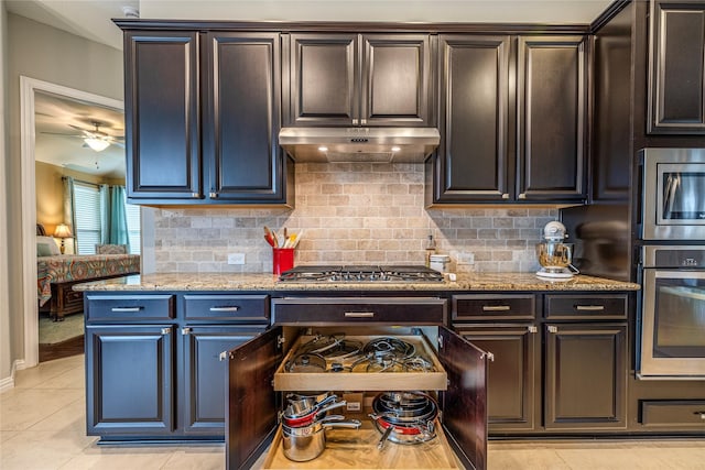 kitchen featuring appliances with stainless steel finishes, under cabinet range hood, light stone counters, decorative backsplash, and light tile patterned floors