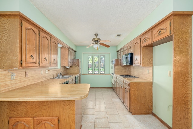 kitchen featuring black microwave, light countertops, stainless steel gas stovetop, backsplash, and a sink