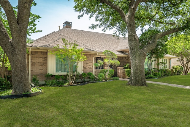 view of front facade with brick siding, a chimney, a front lawn, and roof with shingles