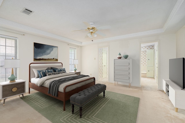 bedroom featuring a tray ceiling, light colored carpet, ensuite bathroom, and a ceiling fan