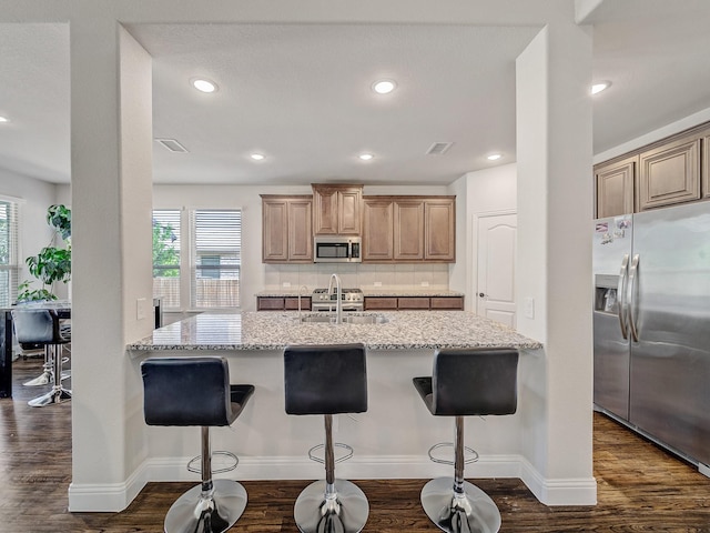 1316 Brentfield Dr, Anna, TX 75409 - kitchen with appliances with stainless steel finishes, light stone counters, dark wood-style flooring, a breakfast bar, and tasteful backsplash