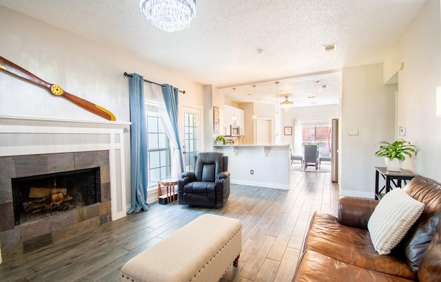 8200 Edgewater Dr, Frisco, TX 75034 - living area featuring a textured ceiling, light wood-style floors, a tiled fireplace, a chandelier, and baseboards
