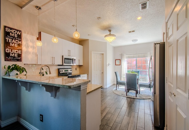 8200 Edgewater Dr, Frisco, TX 75034 - kitchen with stainless steel appliances, a peninsula, a textured ceiling, baseboards, and a kitchen bar