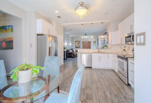 8200 Edgewater Dr, Frisco, TX 75034 - kitchen featuring appliances with stainless steel finishes, open floor plan, light wood-type flooring, and white cabinetry