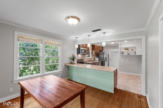 kitchen with stainless steel appliances, light countertops, a peninsula, crown molding, and a sink