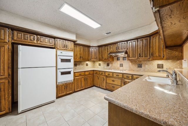 731 N Horne St, Duncanville, TX 75116 - kitchen featuring white appliances, a sink, under cabinet range hood, decorative backsplash, and brown cabinetry