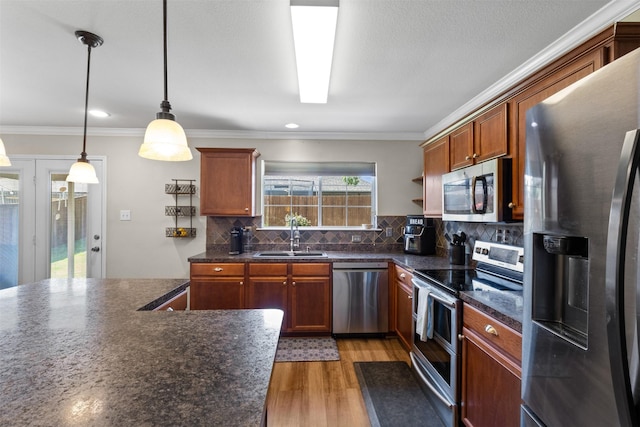 kitchen with appliances with stainless steel finishes, a sink, dark countertops, light wood finished floors, and decorative backsplash