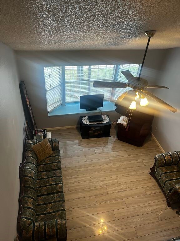 living area featuring light wood-style floors, a ceiling fan, a textured ceiling, and baseboards