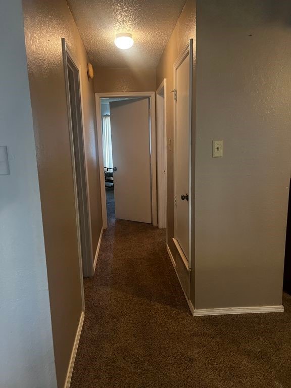 hall with a textured ceiling, carpet floors, and baseboards