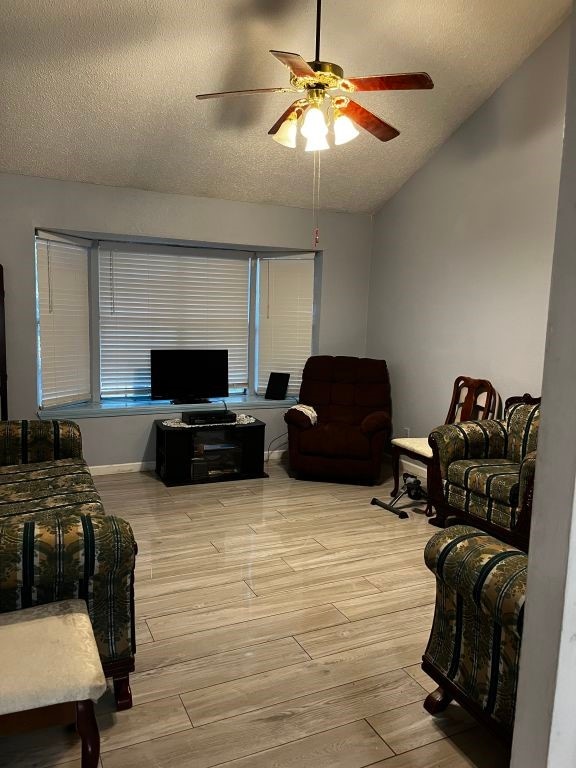 living area with a ceiling fan, a textured ceiling, light wood finished floors, and lofted ceiling